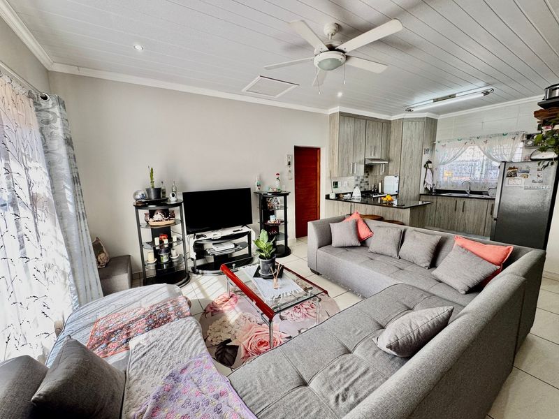 Open-plan living area featuring a kitchen with granite countertops and cabinetry, flowing into a comfortable lounge space with a ceiling fan.