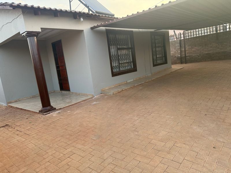 Front exterior view featuring a paved driveway, covered carport, tiled porch area, and security gates on windows and doors.
