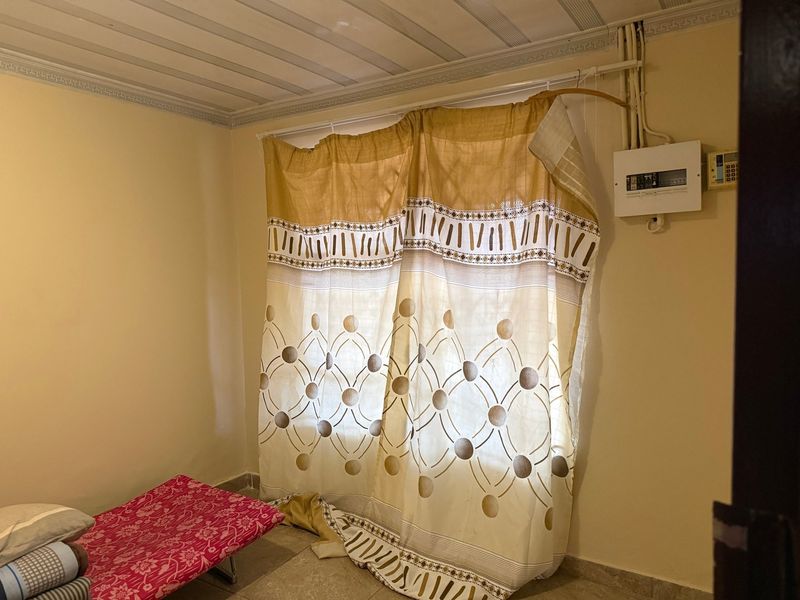 A bedroom interior featuring exposed electrical conduit and a wall-mounted distribution board, with basic ceiling paneling and cornice detailing.