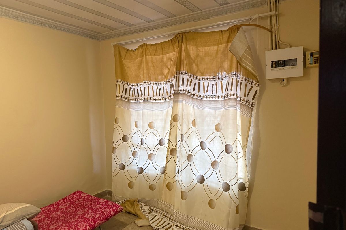 A bedroom interior featuring exposed electrical conduit and a wall-mounted distribution board, with basic ceiling paneling and cornice detailing.