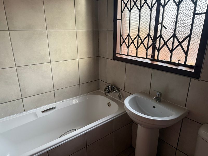 A functional bathroom featuring a standard bathtub, pedestal basin, and tiled walls, equipped with a security gate on the window.