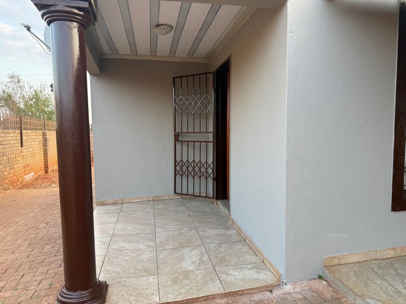 A covered patio area featuring tiled flooring, a decorative support column, and a metal security gate at the entrance.