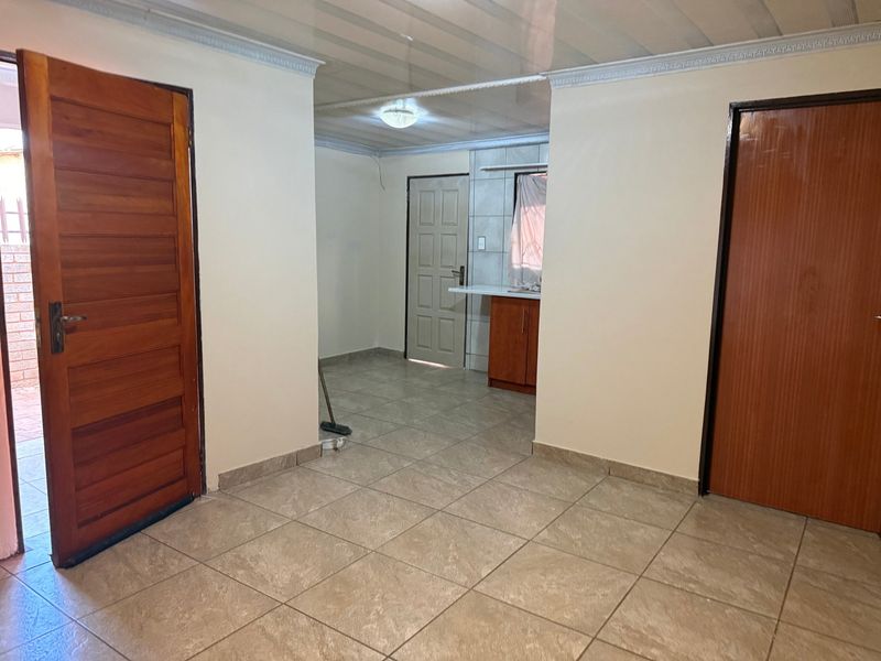 An open-plan living area featuring tiled flooring, solid wood doors, and a compact kitchen corner with built-in cabinetry and countertop.