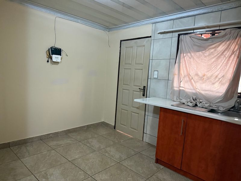 A functional kitchen area featuring tiled flooring, built-in cabinetry with a stainless steel sink, and direct access to an exterior door.