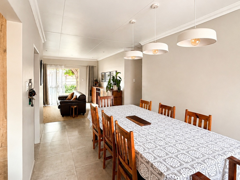 Spacious open-plan dining area featuring neutral tones, modern pendant lighting, tiled flooring, and seamless access to the outdoor patio through sliding glass doors.