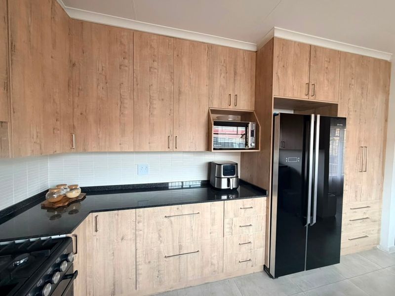 Modern kitchen featuring wood-look cabinetry, black granite countertops, white subway tile backsplash, and dedicated space for a large refrigerator.