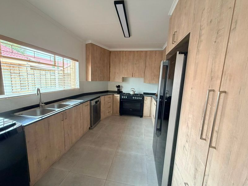 Modern kitchen featuring wood-look cabinetry, black stone countertops, a double basin sink, and a freestanding gas stove with tiled flooring.