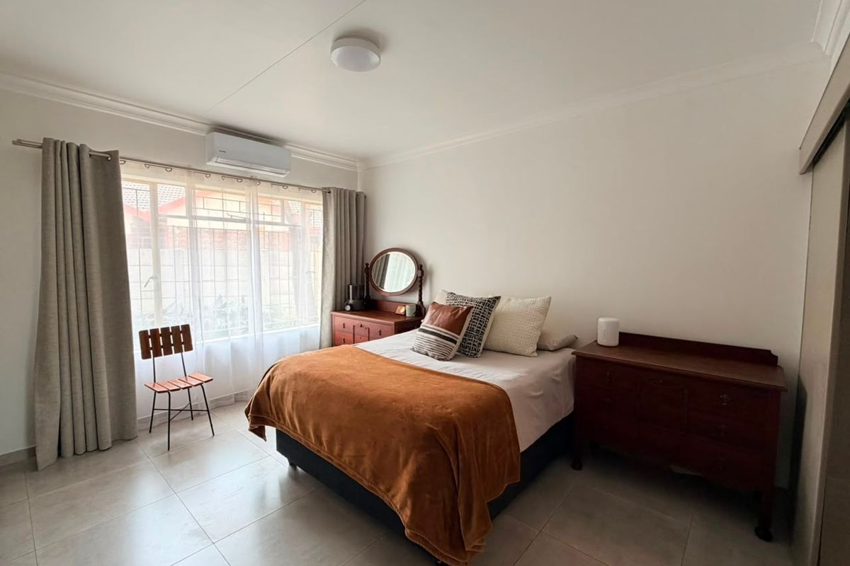 A well-maintained bedroom featuring tiled flooring, a wall-mounted air conditioning unit, and built-in storage, offering a clean and functional living space.