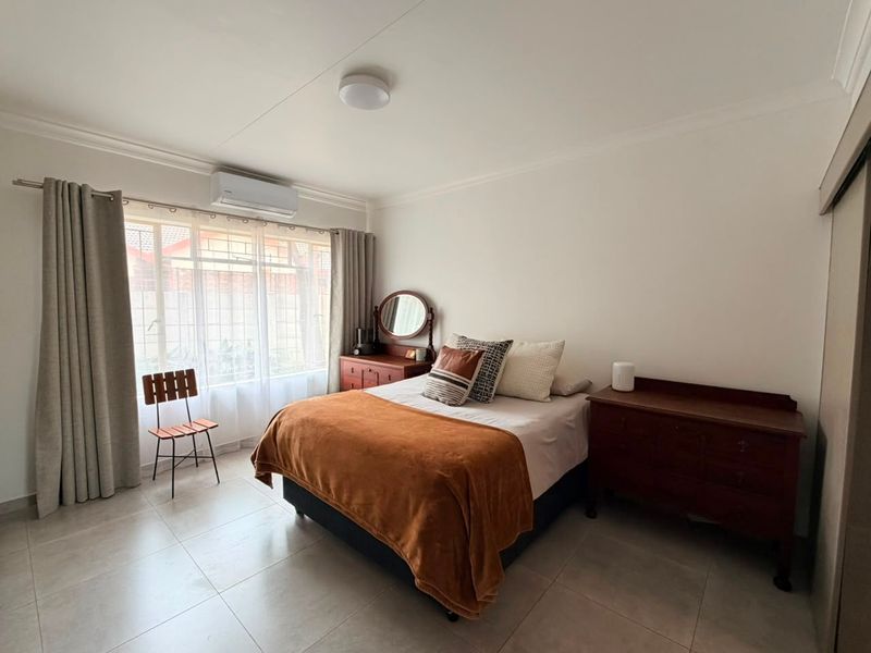 A well-maintained bedroom featuring tiled flooring, a wall-mounted air conditioning unit, and built-in storage, offering a clean and functional living space.