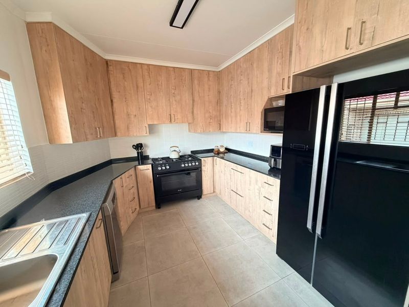 Modern kitchen featuring light wood-look cabinetry, dark granite countertops, a gas stove, and tiled flooring with a clean, functional layout.