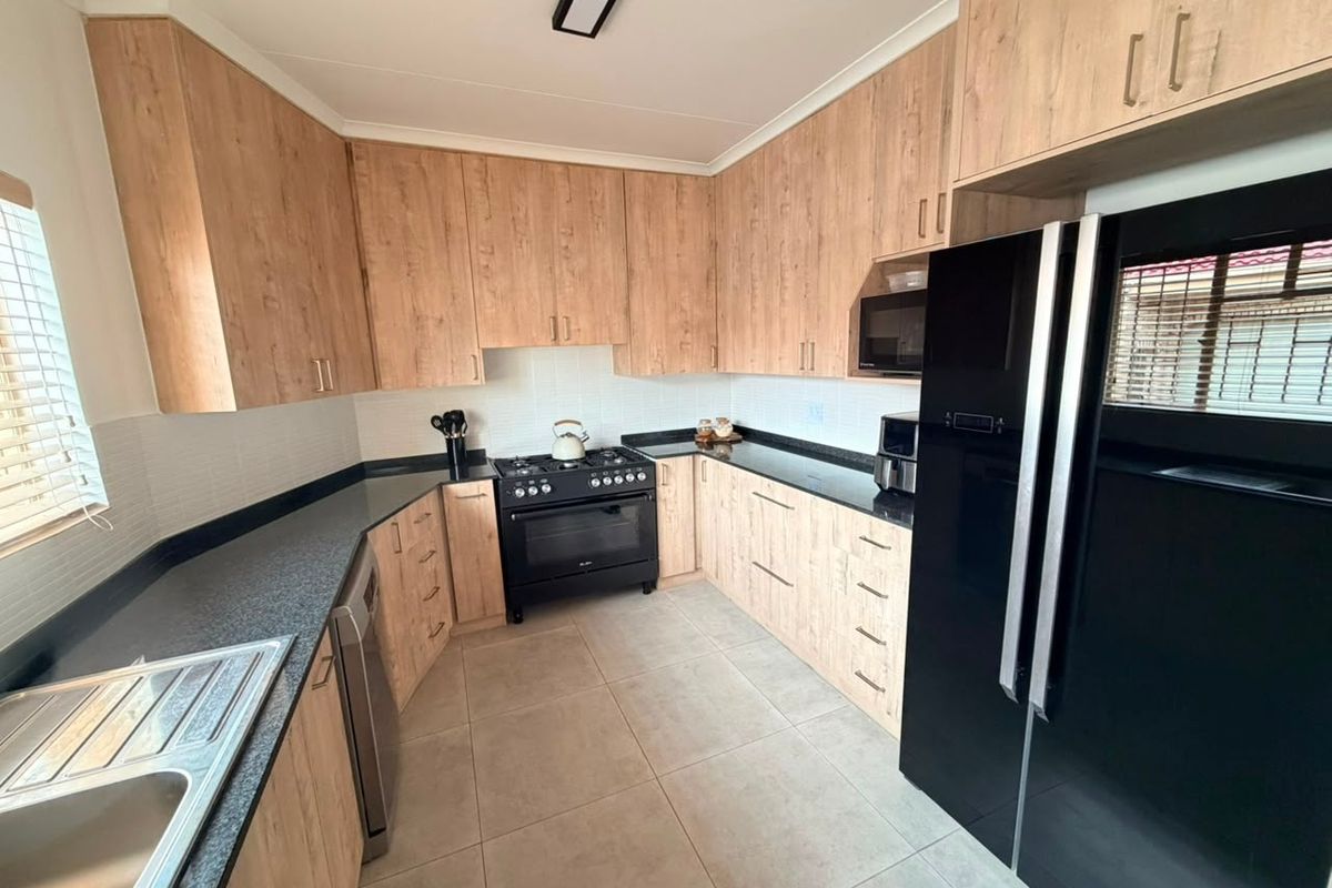 Modern kitchen featuring light wood-look cabinetry, dark granite countertops, a gas stove, and tiled flooring with a clean, functional layout.