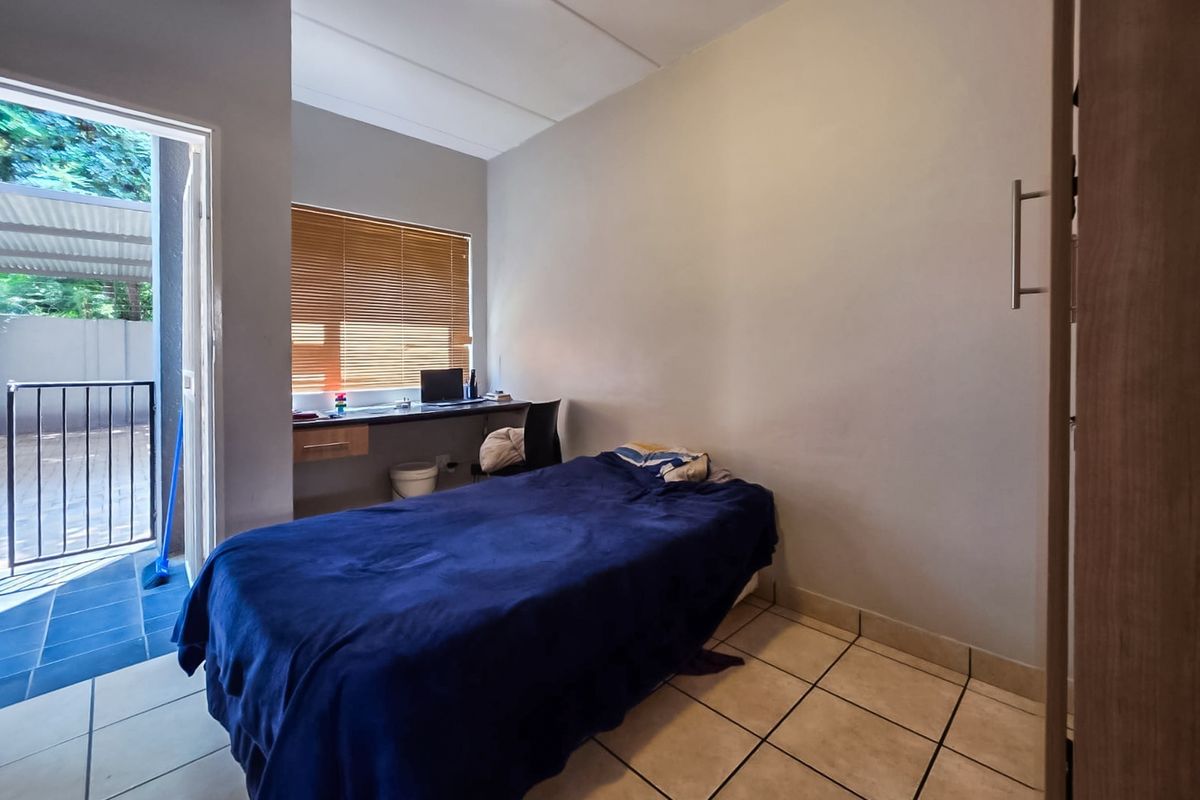 A functional bedroom featuring tiled flooring, a built-in desk, and direct access to an outdoor patio area through a sliding door.