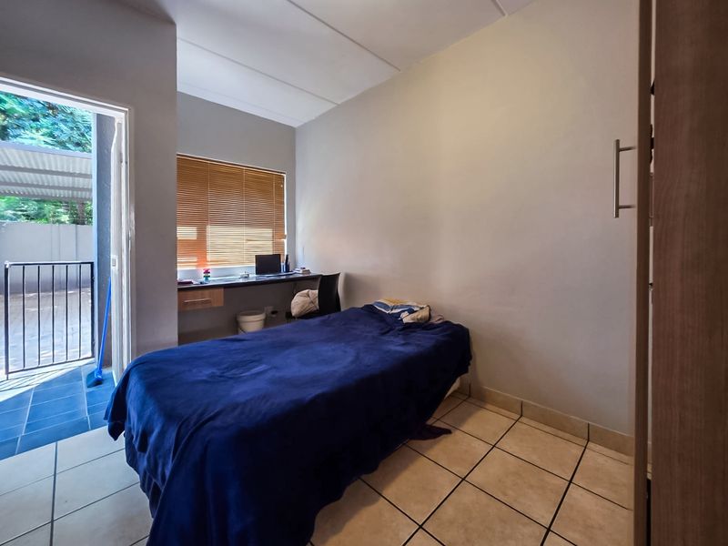 A functional bedroom featuring tiled flooring, a built-in desk, and direct access to an outdoor patio area through a sliding door.