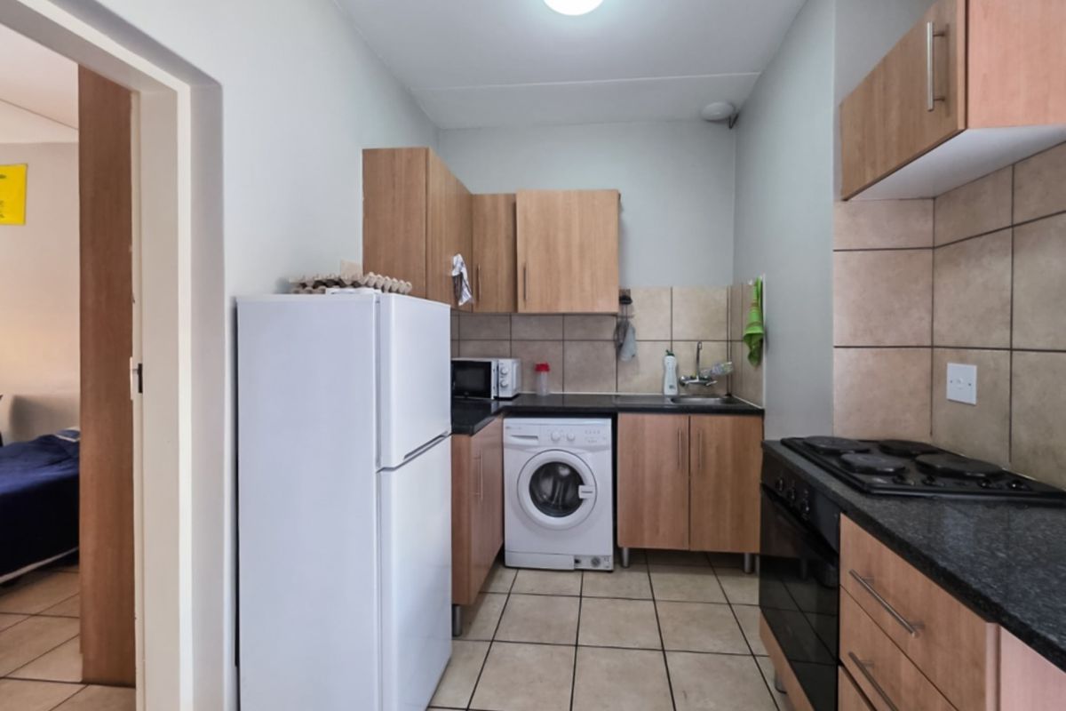 Compact kitchen featuring wood-finish cabinetry, tiled backsplash, integrated hob and oven, and tiled flooring, providing a functional workspace.