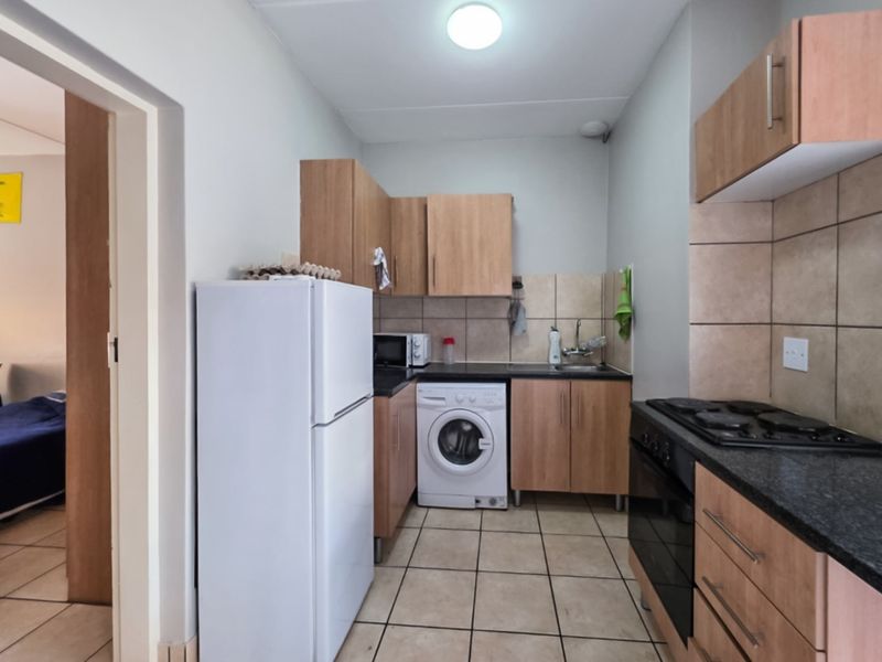 Compact kitchen featuring wood-finish cabinetry, tiled backsplash, integrated hob and oven, and tiled flooring, providing a functional workspace.