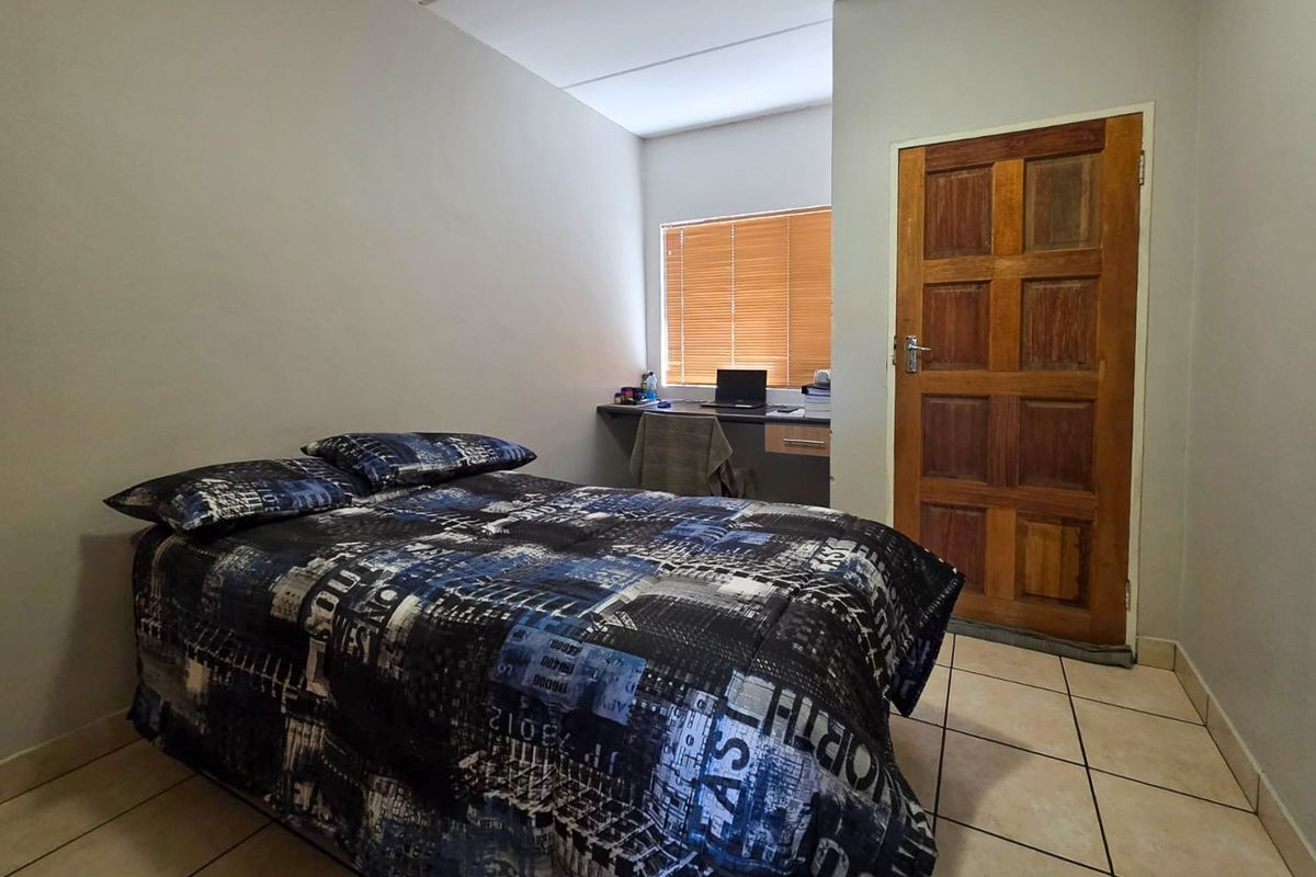 A functional bedroom featuring tiled flooring, a built-in desk area, and a wooden door, providing a practical space for rest and study.