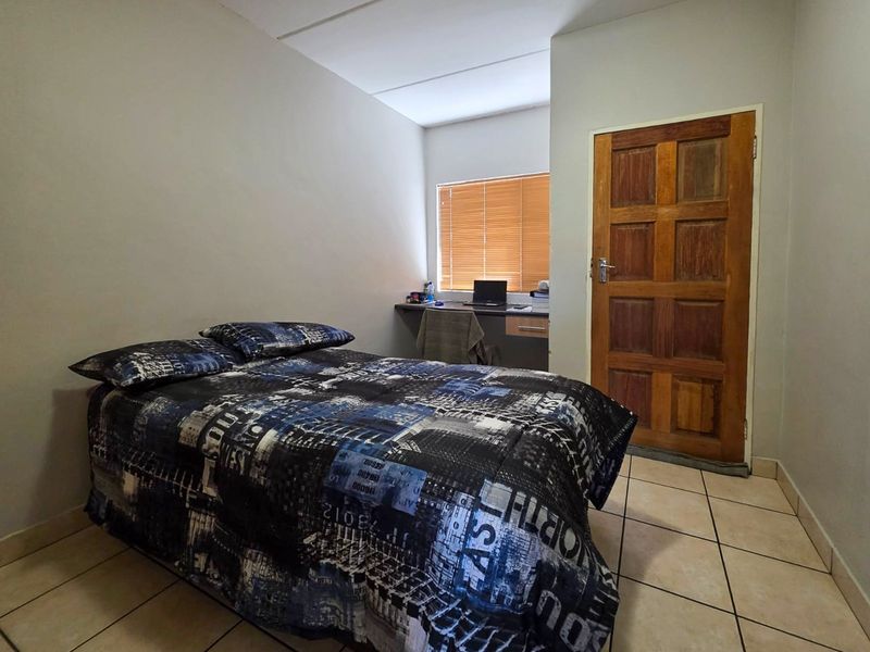 A functional bedroom featuring tiled flooring, a built-in desk area, and a wooden door, providing a practical space for rest and study.