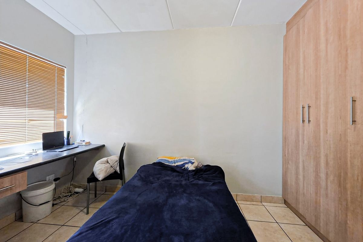 A functional bedroom featuring tiled flooring, built-in cupboards, and a built-in desk area with venetian blinds.