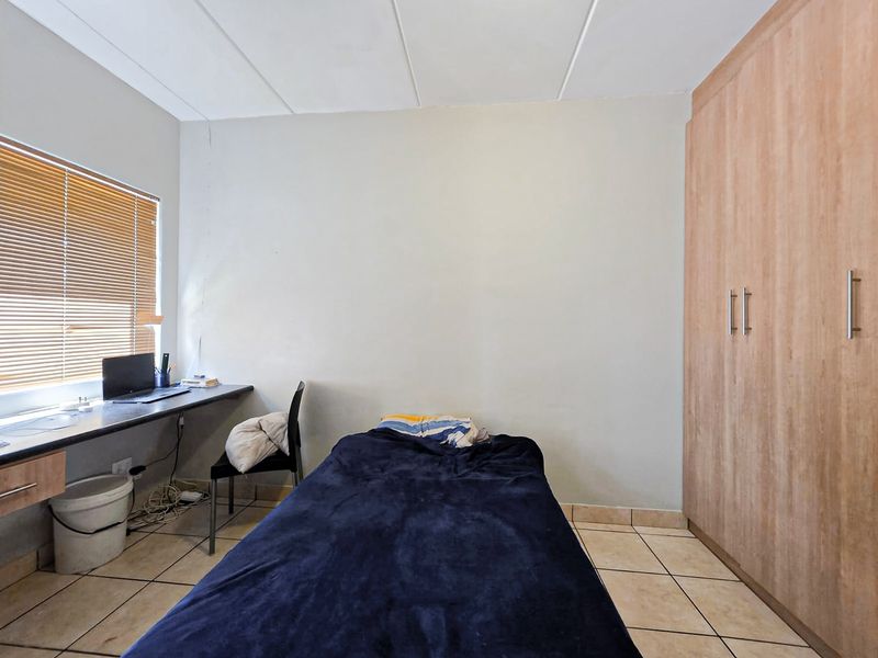 A functional bedroom featuring tiled flooring, built-in cupboards, and a built-in desk area with venetian blinds.