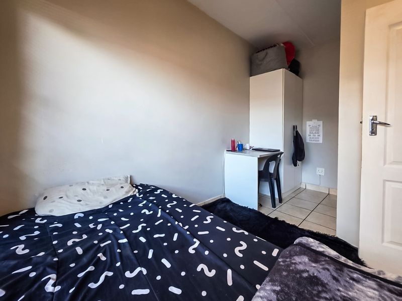 A compact bedroom featuring tiled flooring, a built-in wardrobe, and neutral wall finishes, providing a functional living space.
