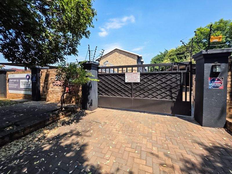 Front entrance of the apartment complex featuring a secure gated access point, brick boundary wall, and electric fencing for enhanced security.