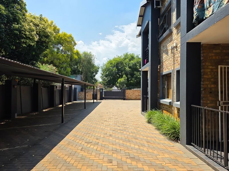 Exterior view of the apartment complex featuring a paved driveway, covered carport parking, and brick building facade with security access.