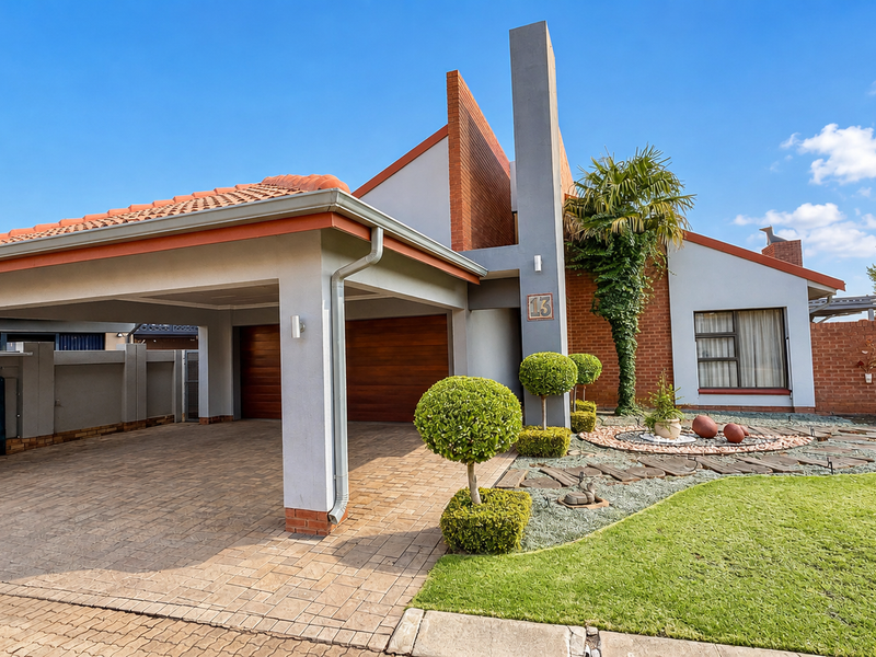 A well-maintained front exterior featuring a spacious double carport, brick paving, a tiled roof, and a neatly landscaped garden with a modern facade.