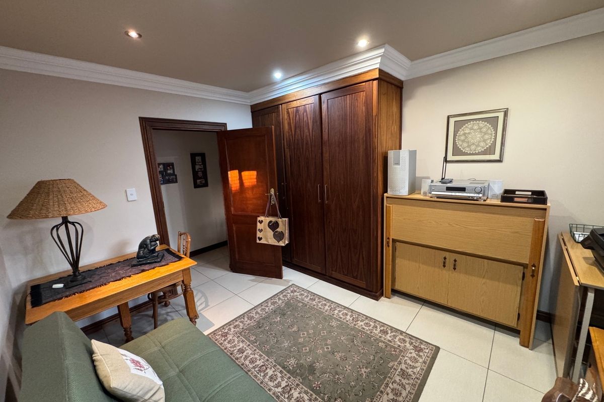 A well-maintained bedroom featuring built-in wooden wardrobes, tiled flooring, and recessed downlighting, offering a functional and neutral living space.