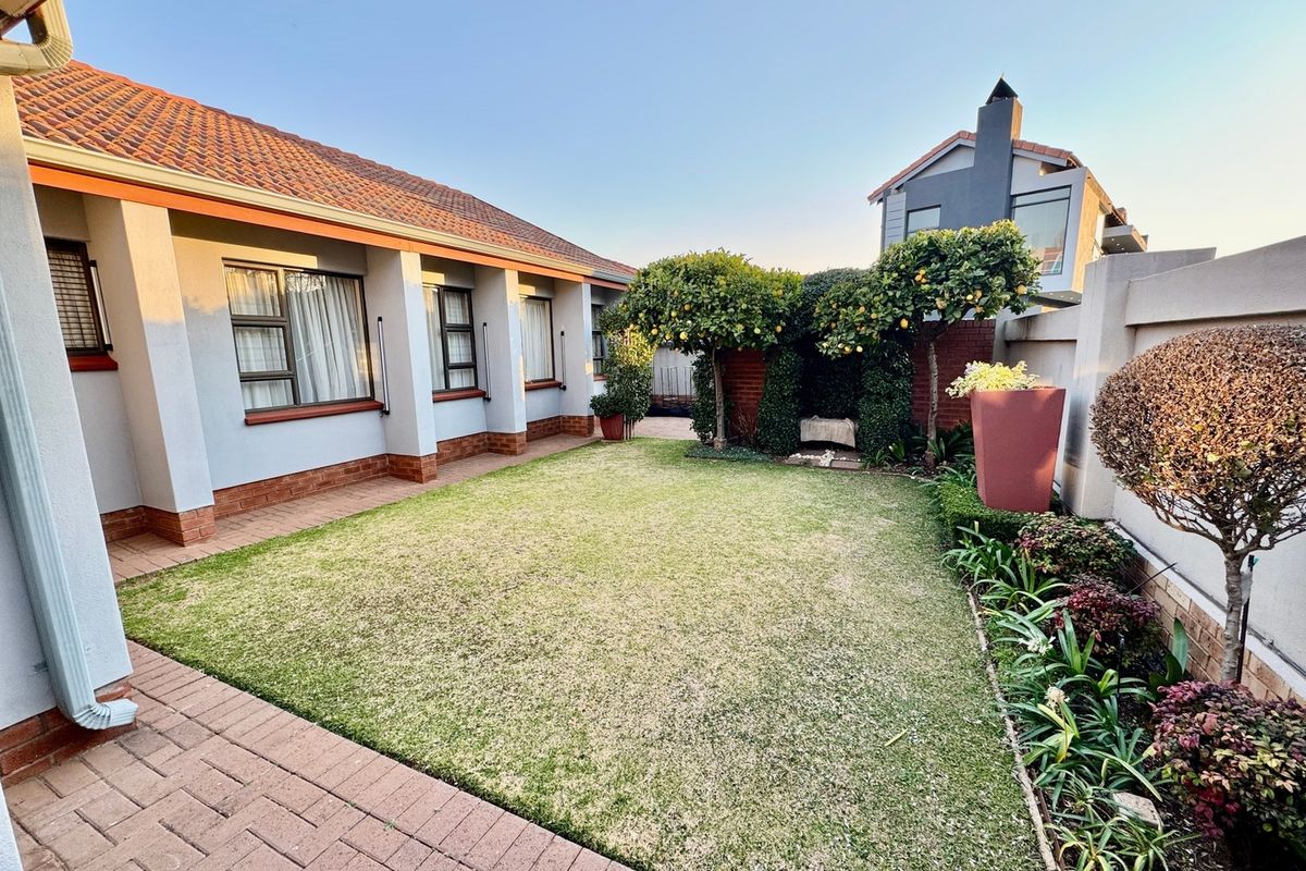 A well-maintained rear garden featuring a paved patio area, manicured lawn, and established perimeter boundary walls.