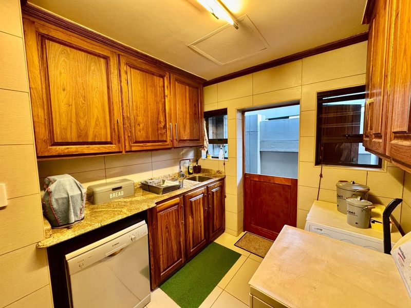 A functional scullery featuring wooden cabinetry, granite countertops, a stainless steel sink, and direct access to the exterior via a stable door.
