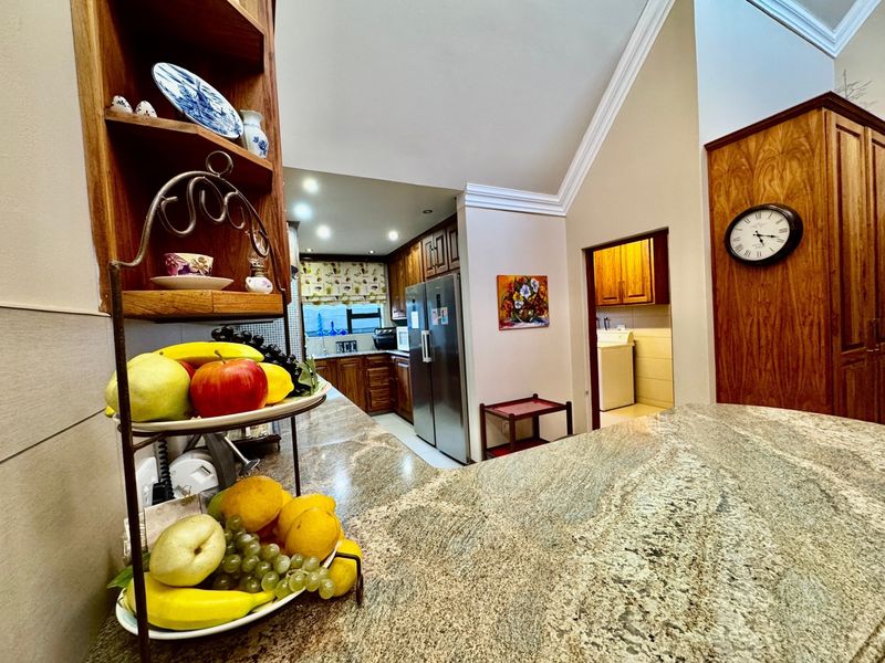 A well-appointed kitchen featuring granite countertops, extensive wooden cabinetry, and a vaulted ceiling with crown molding, leading into a separate laundry area.