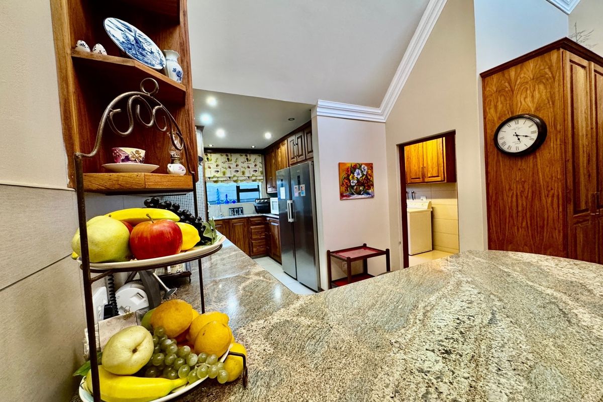 A well-appointed kitchen featuring granite countertops, extensive wooden cabinetry, and a vaulted ceiling with crown molding, leading into a separate laundry area.