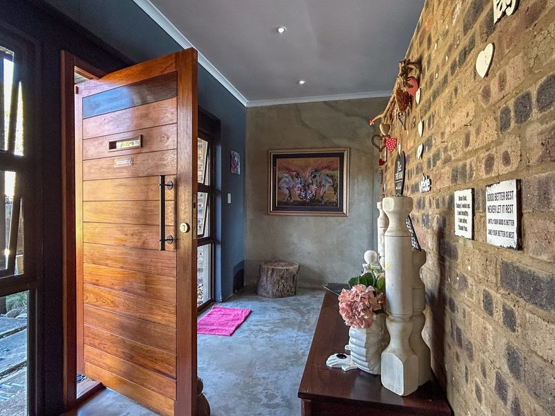 Welcoming entrance hall featuring a solid timber pivot door, exposed brick feature wall, and polished concrete flooring with recessed lighting.