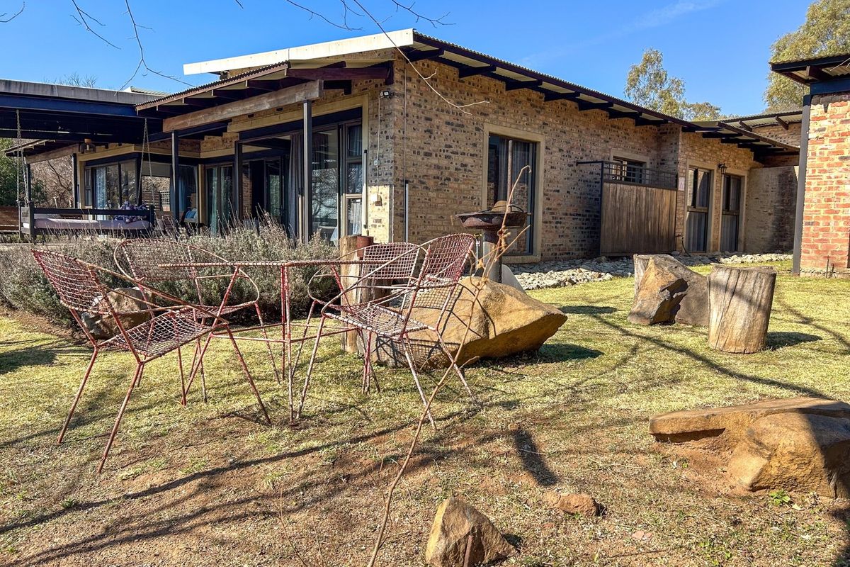 Rear view of a rustic face-brick house featuring a covered patio area and large sliding glass doors opening onto a landscaped garden.