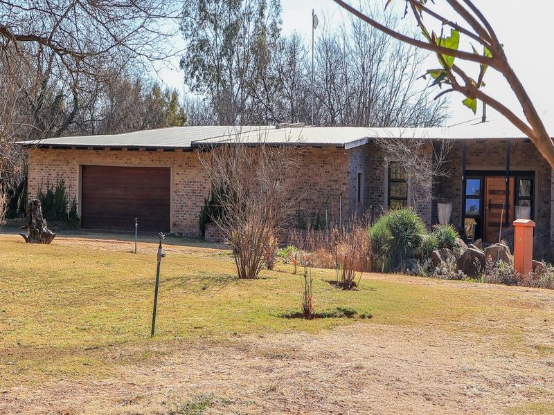 A single-story face brick house featuring a corrugated metal roof, integrated garage, and a spacious front garden area.