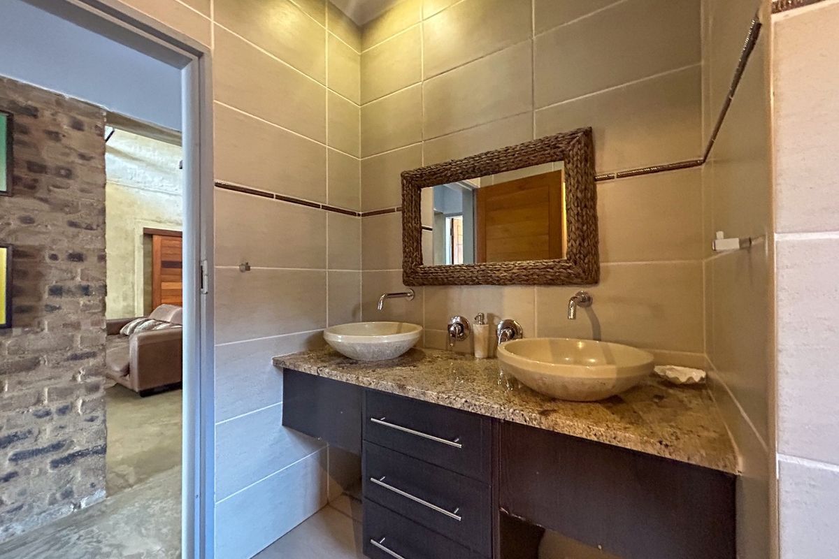A modern bathroom featuring a double vanity with granite countertop, dual vessel sinks, wall-mounted faucets, and neutral wall tiling.