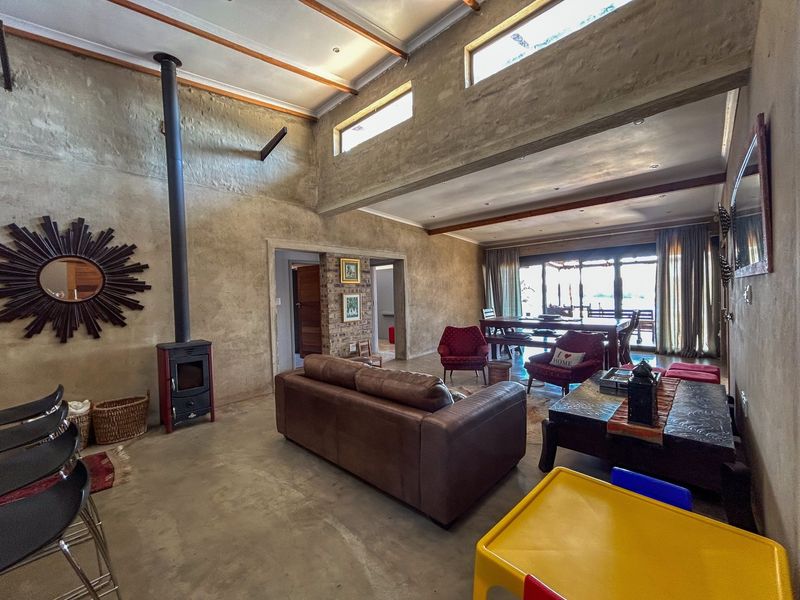 Spacious open-plan living area featuring high ceilings with exposed beams, concrete floors, a freestanding fireplace, and large sliding doors leading to the outdoors.