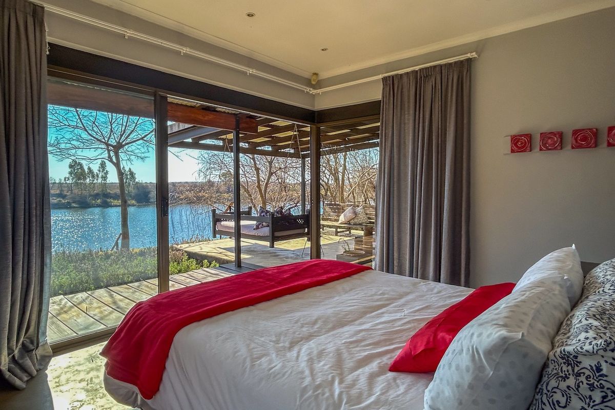 A bright bedroom featuring large sliding glass doors that open onto a covered wooden deck with scenic water views.