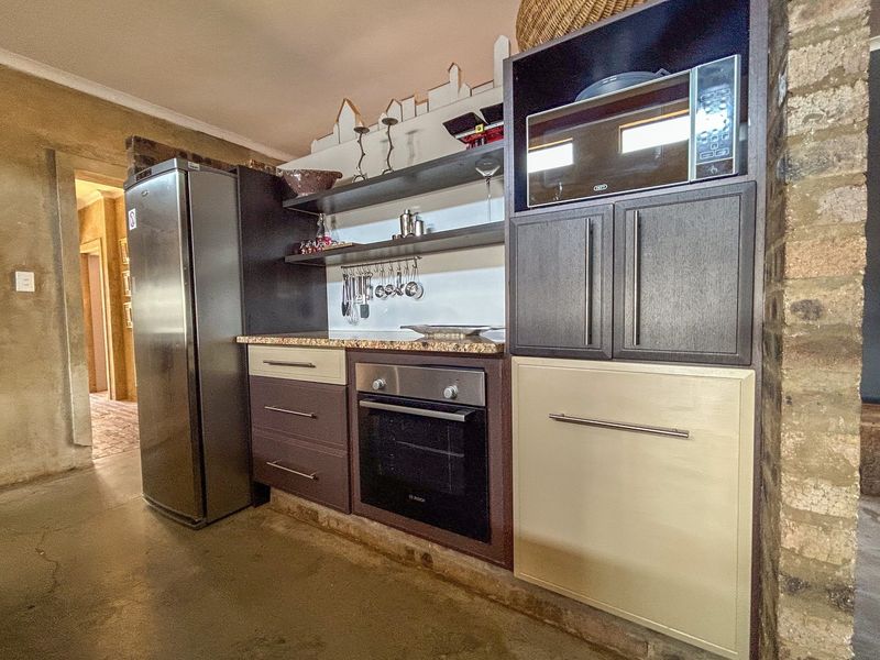 A compact kitchen featuring fitted cabinetry, granite countertops, a built-in oven, and microwave, complemented by an exposed brick wall and polished concrete flooring.
