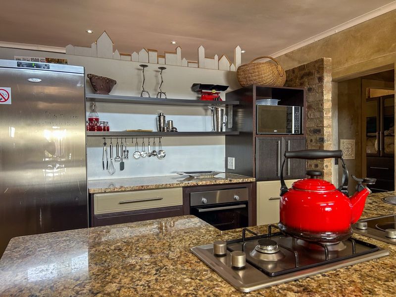 A well-appointed kitchen featuring granite countertops, a built-in oven, gas hob, and an exposed brick feature wall with modern cabinetry and open shelving.