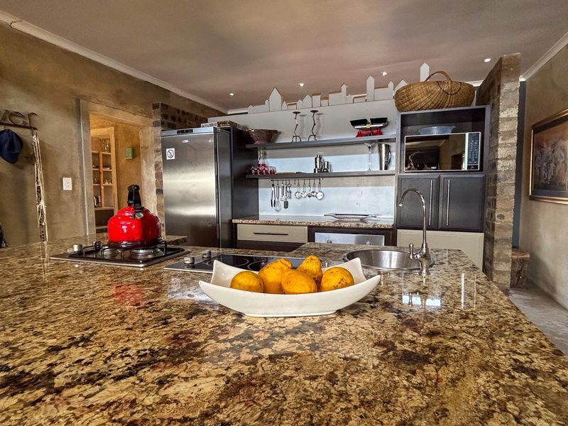 A well-appointed kitchen featuring a large granite-topped island, dual hobs, built-in microwave, and rustic exposed brick accents.