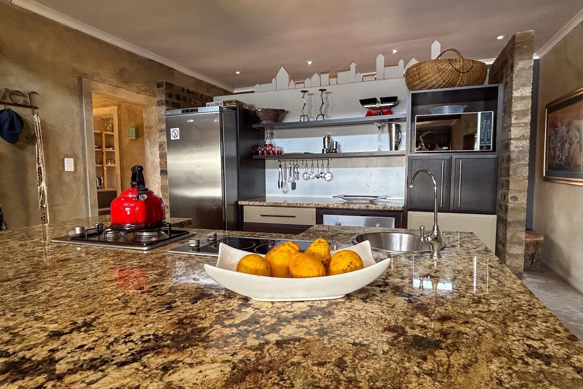 A well-appointed kitchen featuring a large granite-topped island, dual hobs, built-in microwave, and rustic exposed brick accents.