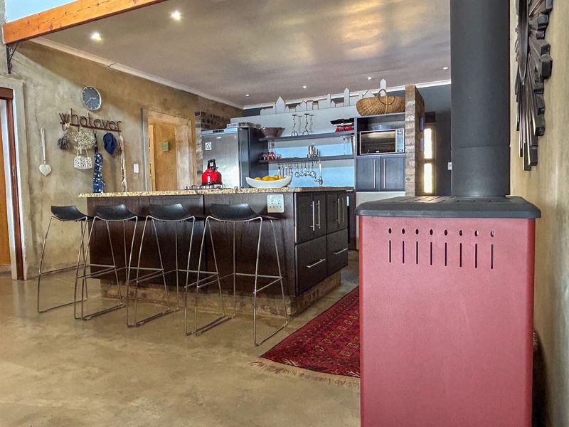 Spacious open-plan kitchen featuring a large island with granite countertops, polished concrete floors, and a prominent freestanding fireplace in the living area.