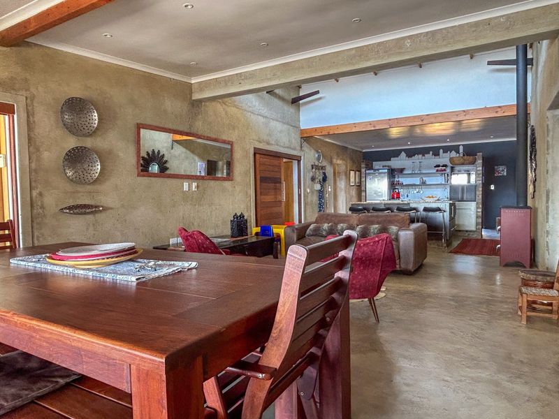 Spacious open-plan living and dining area featuring polished concrete floors, exposed structural beams, and a cozy wood-burning fireplace, flowing into a functional kitchen space.