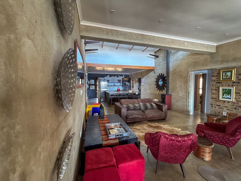 Spacious open-plan living area featuring exposed concrete walls, high ceilings with exposed beams, a wood-burning fireplace, and a connected kitchen with island seating.