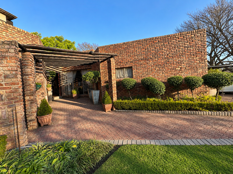 A well-maintained front exterior featuring a classic face brick facade, a timber pergola over the entrance, and a neatly paved driveway with landscaped garden.