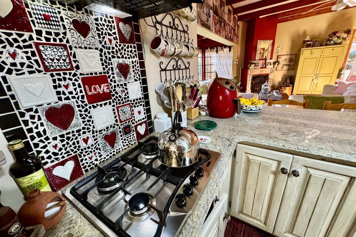 A kitchen area featuring a gas hob, extractor fan, and granite countertops, with a decorative mosaic tile backsplash and exposed wooden ceiling beams.