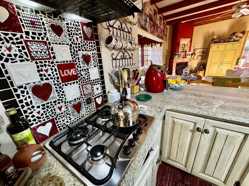 A kitchen area featuring a gas hob, extractor fan, and granite countertops, with a decorative mosaic tile backsplash and exposed wooden ceiling beams.