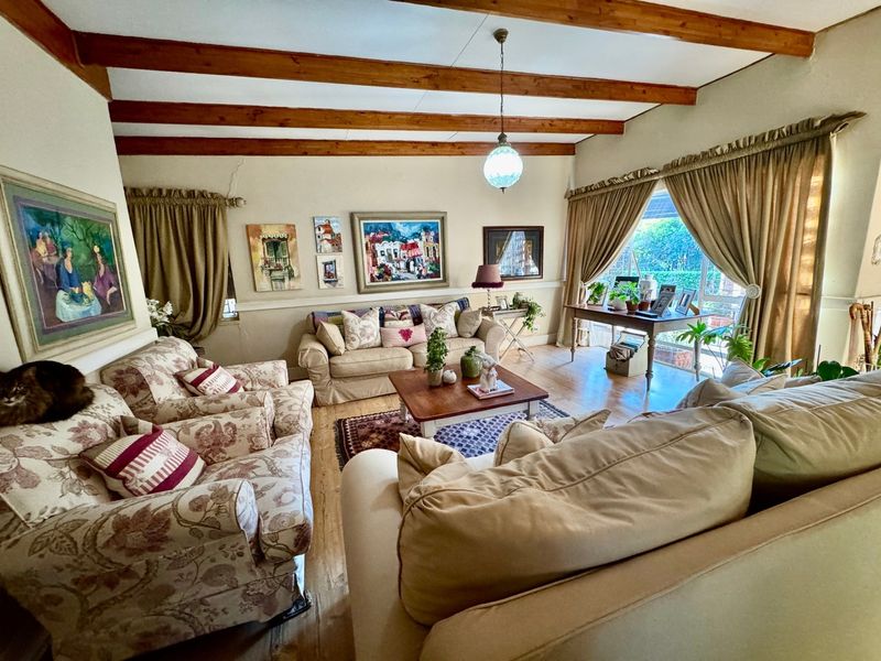 A cozy living room featuring exposed timber ceiling beams, hardwood flooring, and a large sliding glass door providing natural light and garden access.