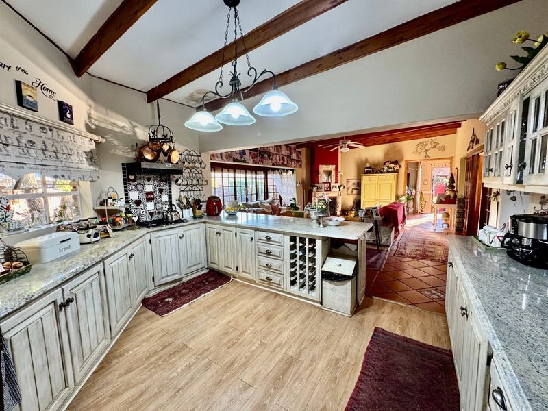 Spacious open-plan kitchen and living area featuring exposed timber beams, granite countertops, and a mix of terracotta and laminate flooring.